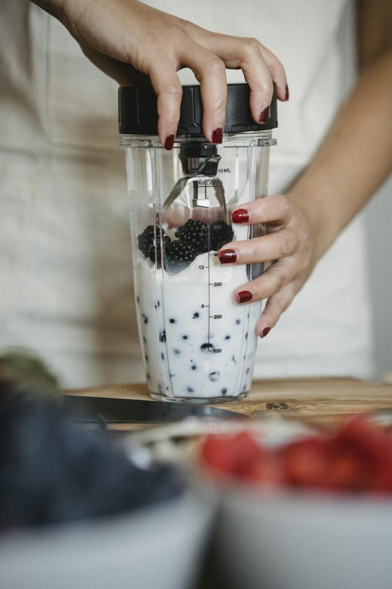 Close-up of a woman making a healthy blackberry smoothie, showcasing hands and blender.