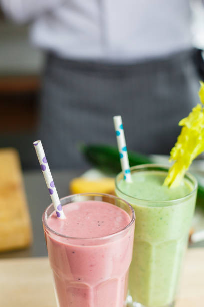 Crop faceless shot of male chef in uniform posing with two fresh smoothies.